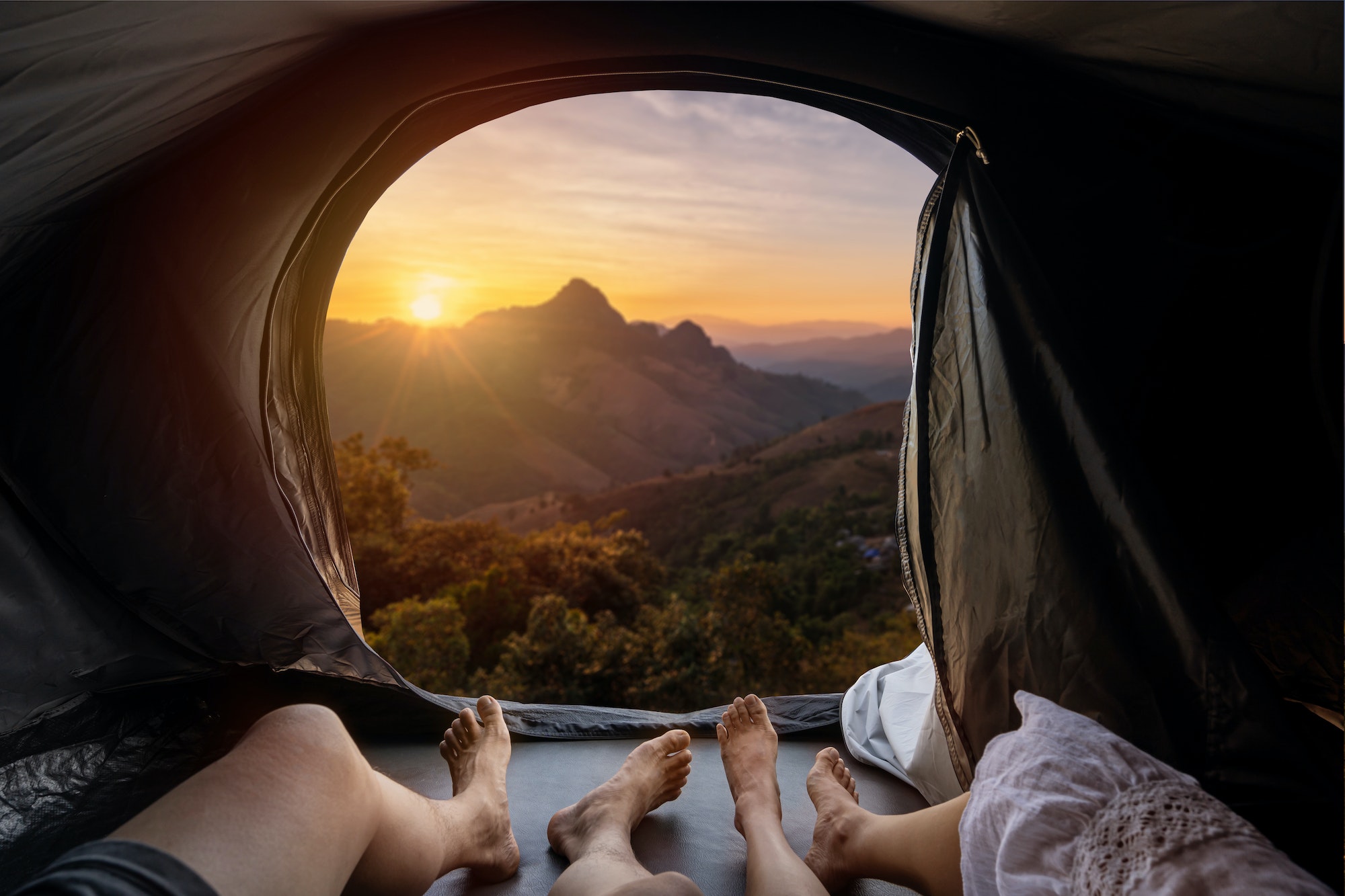 Young couple lying in camping tent and looking at sunset over the mountain
