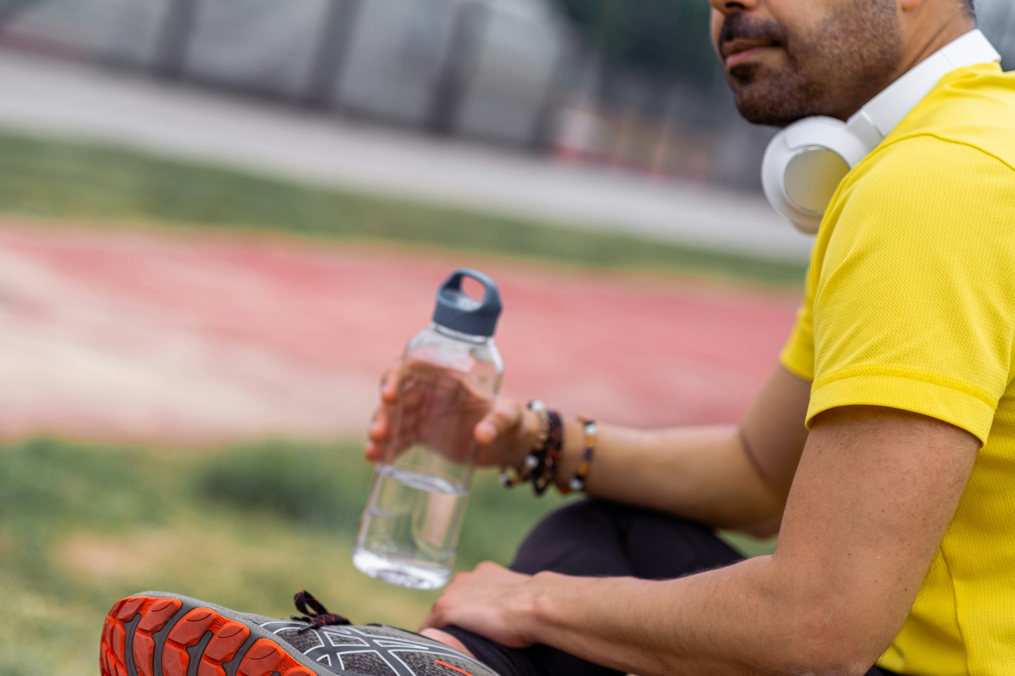Athlete in colorful t-shirt, with headphones and water bottle during training break at sports arena